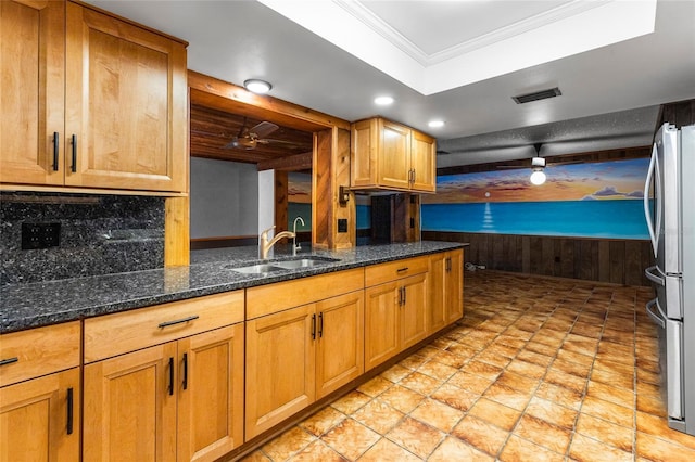 kitchen featuring stainless steel refrigerator, sink, tasteful backsplash, dark stone counters, and ornamental molding