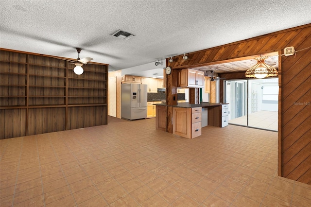 kitchen with pendant lighting, backsplash, stainless steel refrigerator with ice dispenser, wooden walls, and ceiling fan