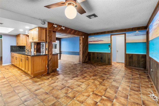 kitchen featuring a skylight, ceiling fan, backsplash, wood walls, and a textured ceiling