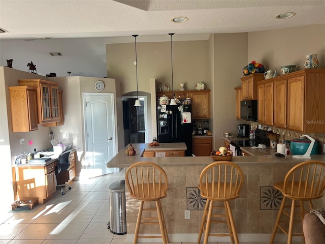 kitchen featuring black appliances, light tile patterned flooring, kitchen peninsula, a kitchen breakfast bar, and decorative light fixtures