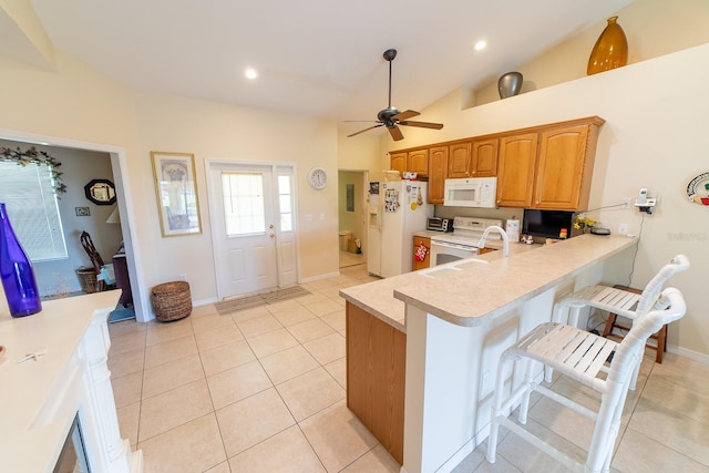 kitchen with white appliances, light tile patterned flooring, kitchen peninsula, vaulted ceiling, and a breakfast bar area