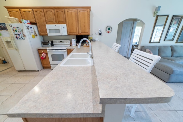 kitchen featuring kitchen peninsula, sink, a kitchen bar, light tile patterned floors, and white appliances