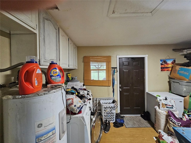 laundry room featuring electric water heater, cabinets, light hardwood / wood-style flooring, and washer and clothes dryer