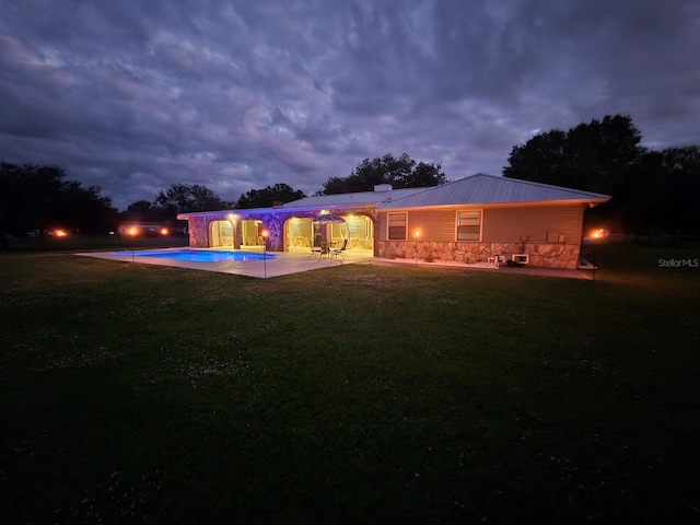 back house at dusk featuring a yard and a patio