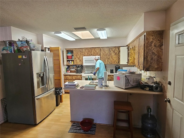 kitchen with light hardwood / wood-style flooring, kitchen peninsula, a textured ceiling, white appliances, and a breakfast bar