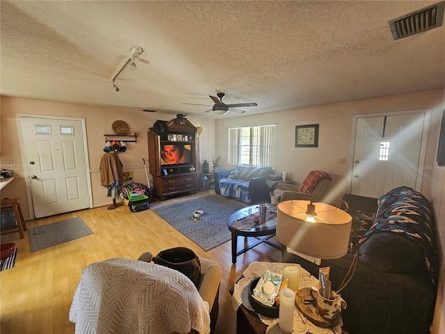 living room featuring rail lighting, ceiling fan, wood-type flooring, and a textured ceiling