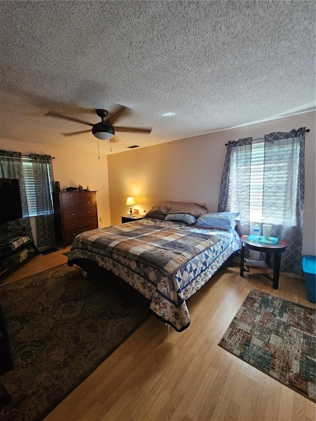 bedroom with ceiling fan, light wood-type flooring, and a textured ceiling