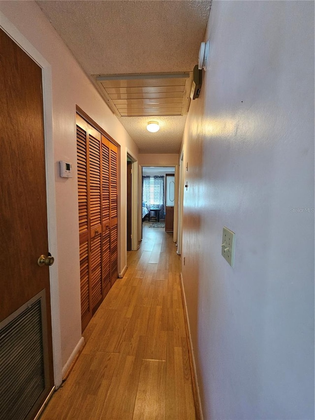 hall with a textured ceiling and light hardwood / wood-style flooring