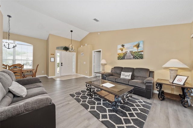 living room with hardwood / wood-style flooring, a notable chandelier, and vaulted ceiling