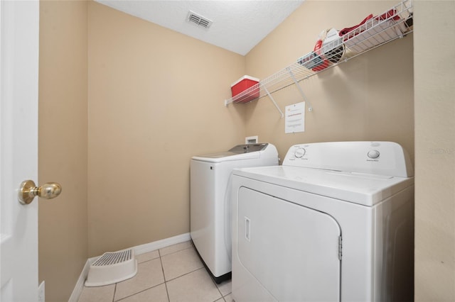 washroom with washing machine and clothes dryer, light tile patterned flooring, and a textured ceiling