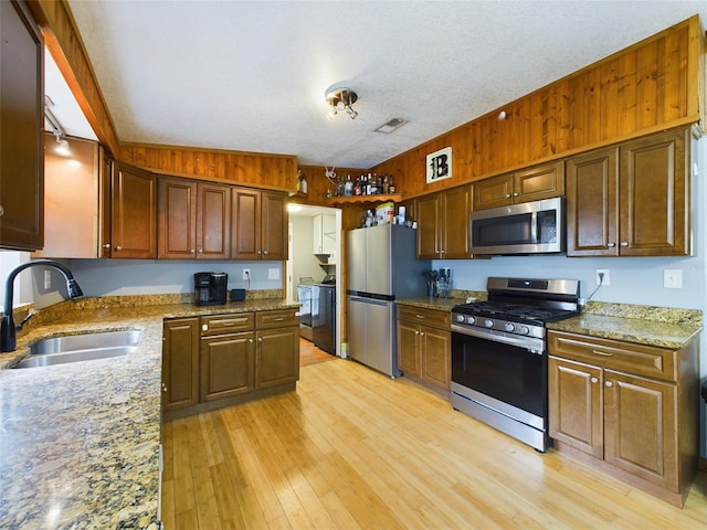 kitchen with sink, light hardwood / wood-style flooring, a textured ceiling, wooden walls, and appliances with stainless steel finishes