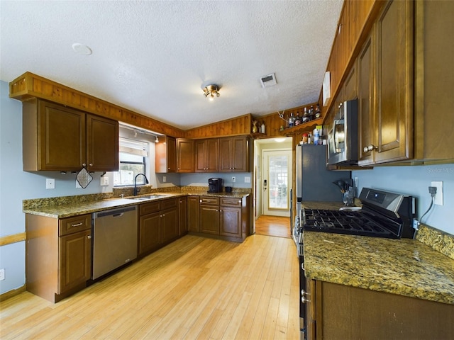 kitchen featuring a textured ceiling, stainless steel appliances, sink, light hardwood / wood-style flooring, and stone counters