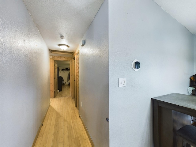 corridor with a textured ceiling and light hardwood / wood-style flooring