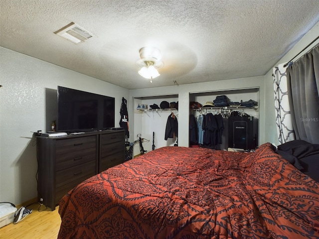 bedroom featuring two closets, ceiling fan, light hardwood / wood-style flooring, and a textured ceiling