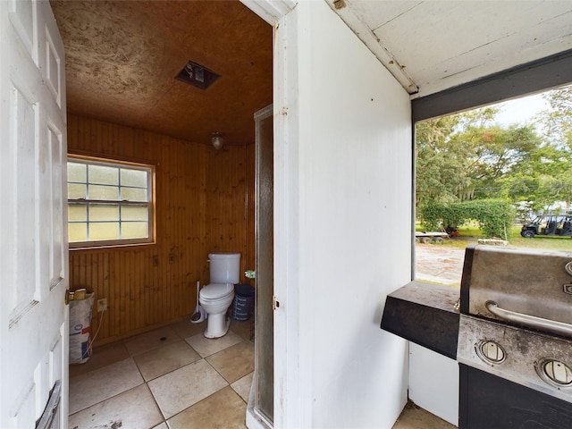 bathroom with tile patterned floors, wooden walls, and toilet