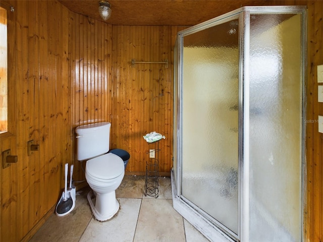 bathroom featuring tile patterned flooring, toilet, a shower with door, and wood walls