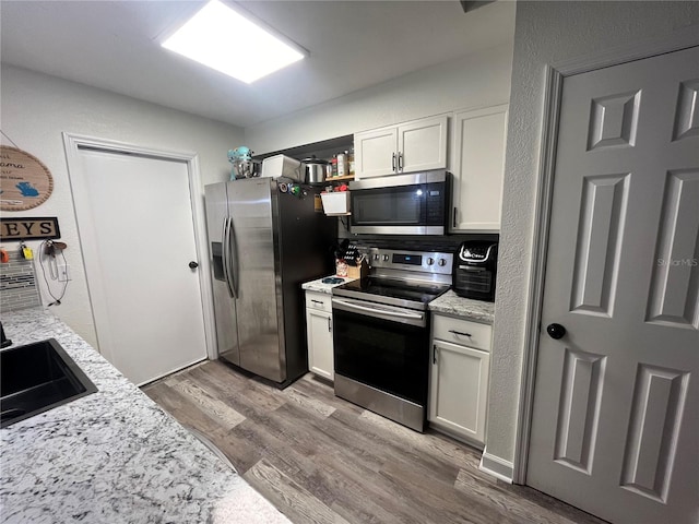 kitchen featuring light stone countertops, sink, stainless steel appliances, light hardwood / wood-style floors, and white cabinets