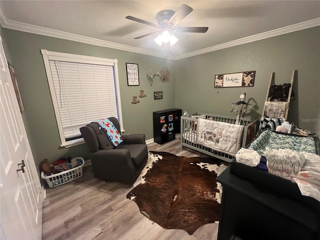 bedroom featuring ceiling fan, crown molding, a crib, and light wood-type flooring