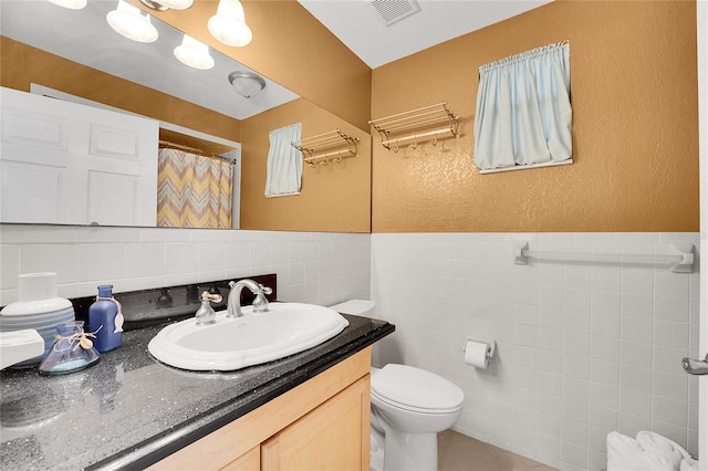 bathroom featuring walk in shower, vanity, tile walls, and toilet