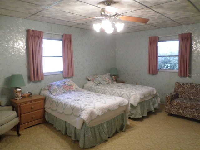 carpeted bedroom with multiple windows, wallpapered walls, and a ceiling fan