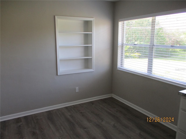 empty room featuring built in shelves, plenty of natural light, and dark hardwood / wood-style floors