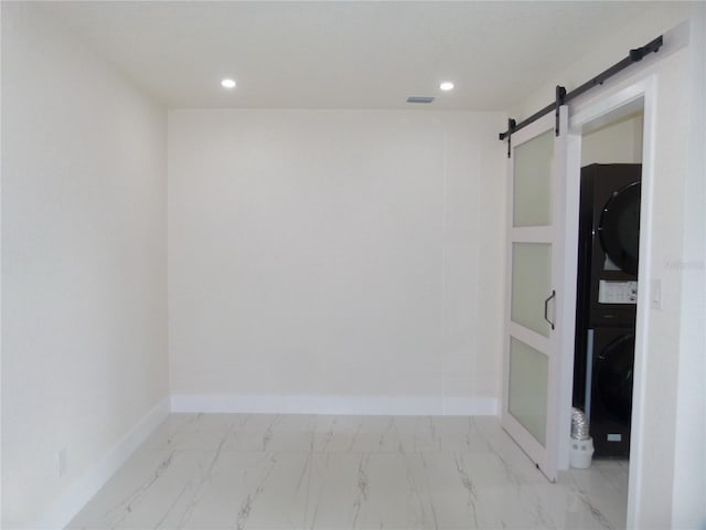 spare room with a barn door and stacked washing maching and dryer