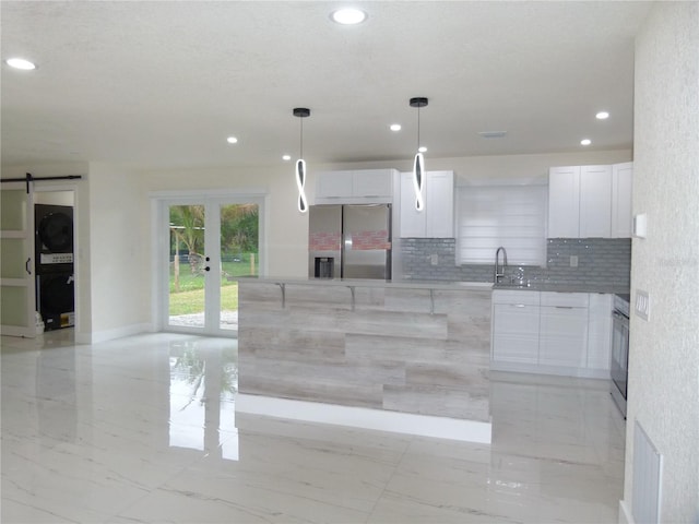 kitchen with hanging light fixtures, a barn door, tasteful backsplash, white cabinetry, and stainless steel appliances