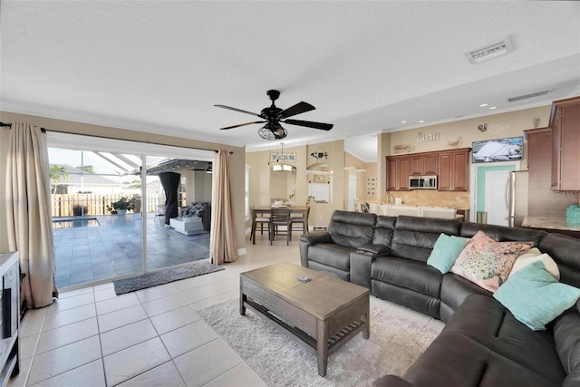 living room with ceiling fan, light tile patterned flooring, and a textured ceiling