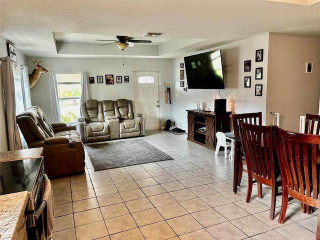 tiled living room with a raised ceiling, ceiling fan, and a textured ceiling