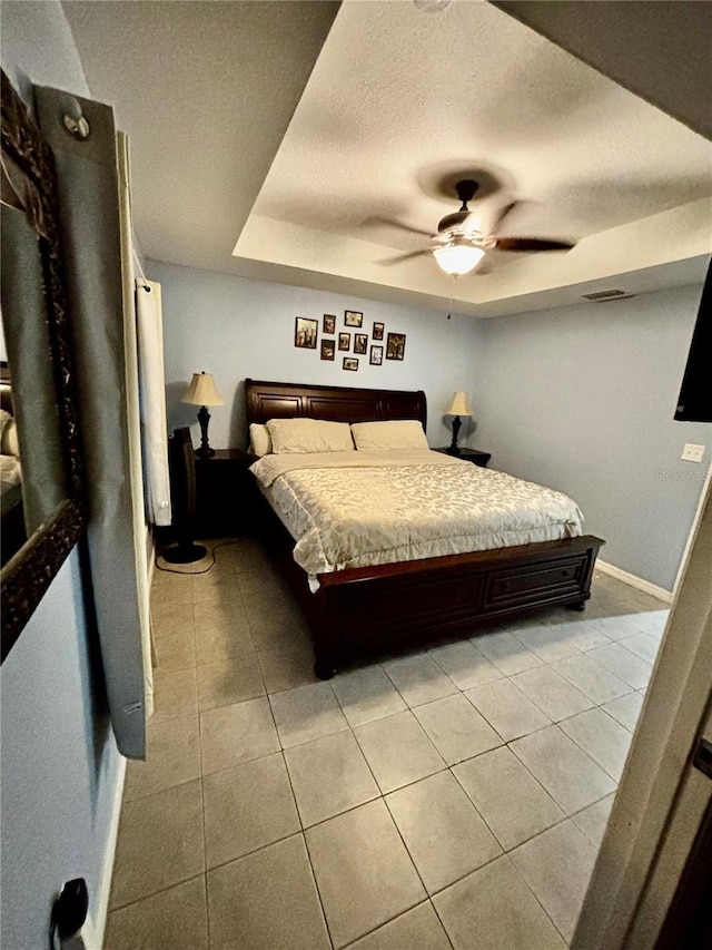 bedroom with ceiling fan, light tile patterned floors, a textured ceiling, and a tray ceiling