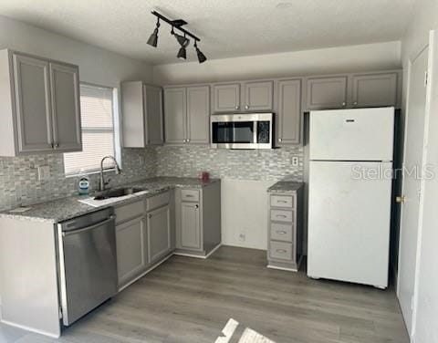 kitchen featuring sink, light hardwood / wood-style flooring, gray cabinets, appliances with stainless steel finishes, and tasteful backsplash