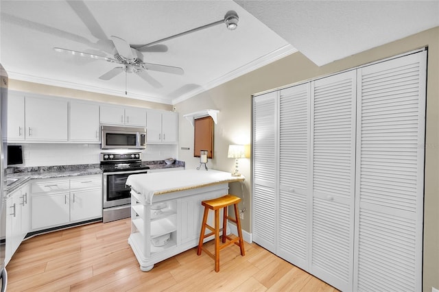 kitchen featuring appliances with stainless steel finishes, white cabinetry, tasteful backsplash, a kitchen breakfast bar, and light wood-type flooring