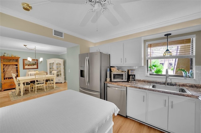 kitchen with light hardwood / wood-style floors, hanging light fixtures, white cabinets, sink, and stainless steel appliances