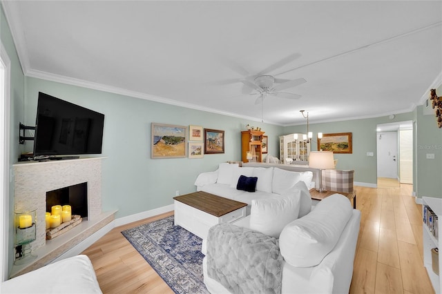 living room featuring crown molding, light hardwood / wood-style floors, ceiling fan with notable chandelier, and a stone fireplace