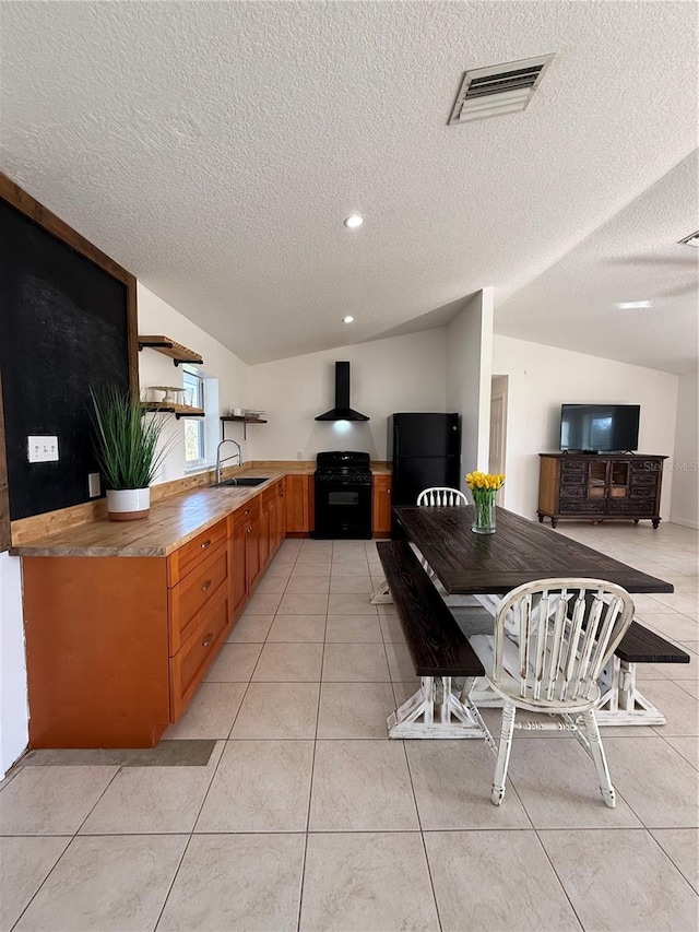 kitchen with lofted ceiling, wall chimney range hood, light tile patterned floors, and black appliances