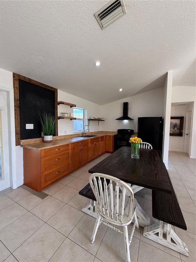 kitchen with wall chimney range hood, light tile patterned floors, a textured ceiling, and black appliances