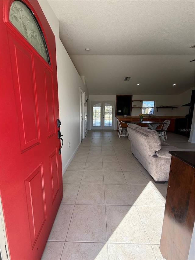 hall featuring french doors, light tile patterned flooring, and a textured ceiling