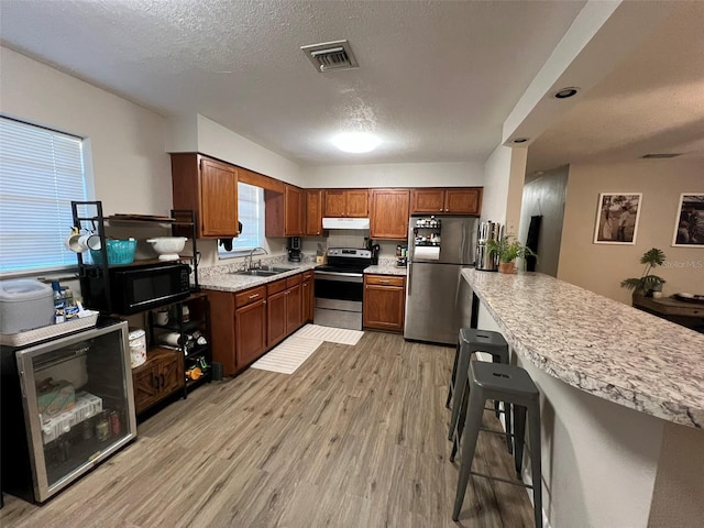 kitchen featuring a kitchen bar, sink, a textured ceiling, stainless steel appliances, and light hardwood / wood-style floors