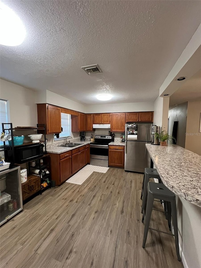 kitchen featuring sink, light hardwood / wood-style flooring, stainless steel appliances, and a textured ceiling