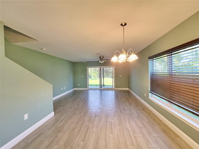 empty room featuring ceiling fan with notable chandelier and light hardwood / wood-style flooring