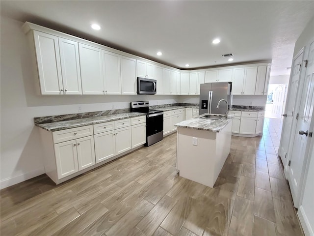 kitchen featuring stone counters, appliances with stainless steel finishes, a kitchen island with sink, and white cabinets