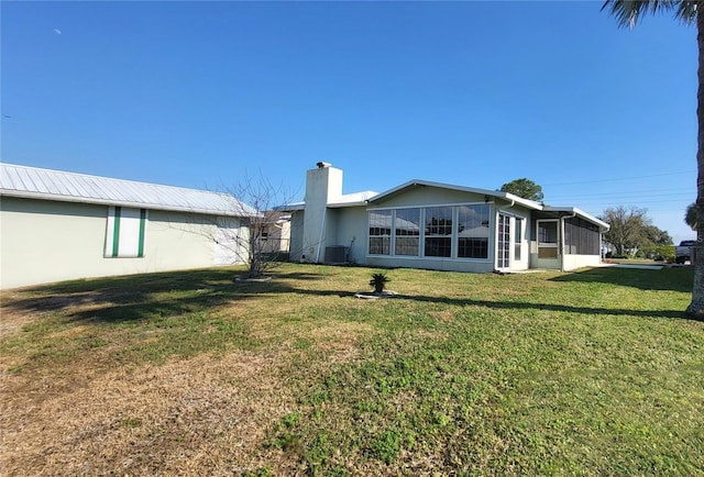 rear view of house with central AC, a sunroom, and a lawn