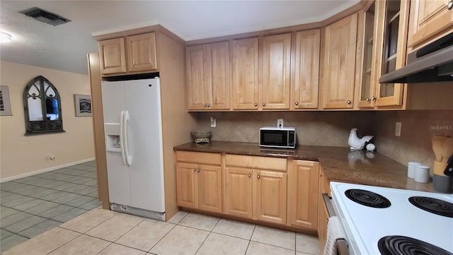 kitchen featuring light tile patterned flooring, white appliances, dark stone counters, and tasteful backsplash