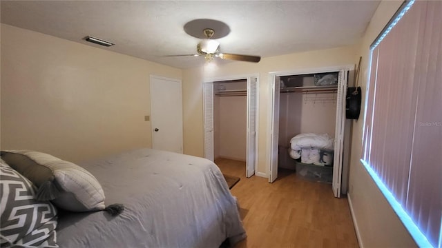 bedroom with ceiling fan, light hardwood / wood-style floors, and two closets