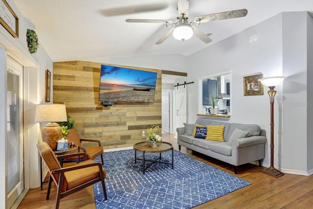 living room with lofted ceiling, a barn door, an accent wall, wood walls, and wood finished floors