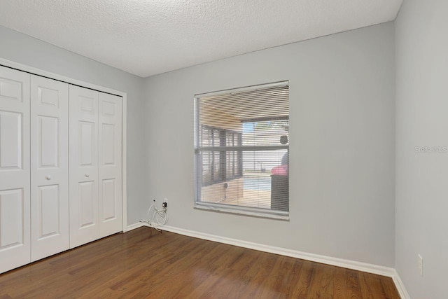 unfurnished bedroom featuring a closet, dark wood finished floors, a textured ceiling, and baseboards