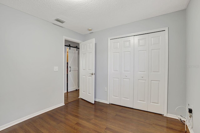 unfurnished bedroom featuring a barn door, visible vents, dark wood finished floors, baseboards, and a textured ceiling