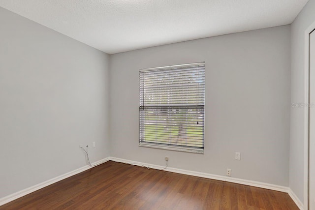 spare room with a textured ceiling, wood finished floors, and baseboards