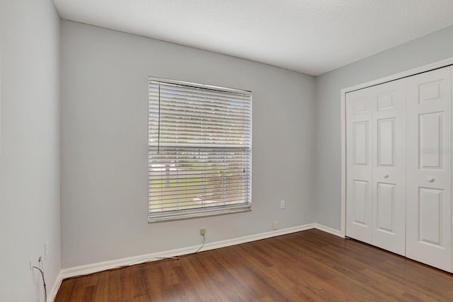 unfurnished bedroom featuring a closet, dark wood finished floors, and baseboards