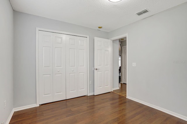 unfurnished bedroom with dark wood-style floors, a closet, visible vents, and baseboards